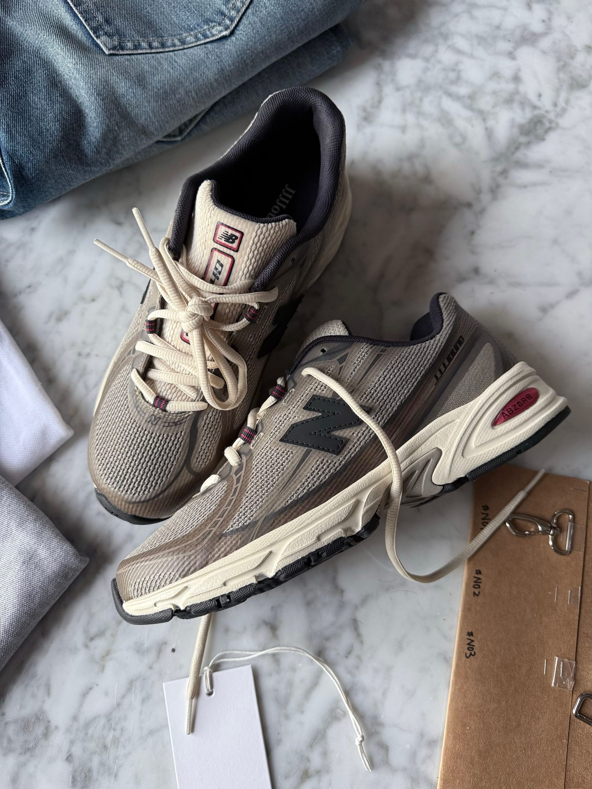 Angled view of the JJJJound x New Balance 740N Mushroom pair on a marble surface, showing the lateral profile, cream midsole and red ABZORB heel callout