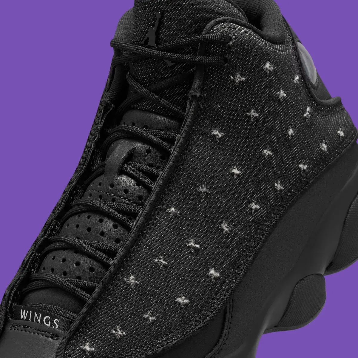 Close-up of the Air Jordan 13 Wings black denim twill upper, distressed X-shaped stitching, WINGS toe branding and the Jumpman on the tongue