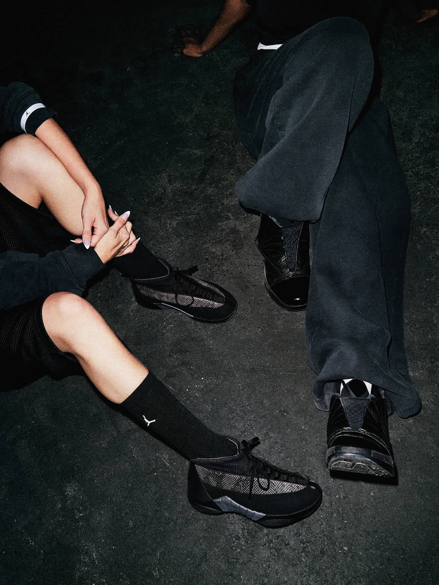 Two models seated on concrete wearing Air Jordan Black Pack sneakers